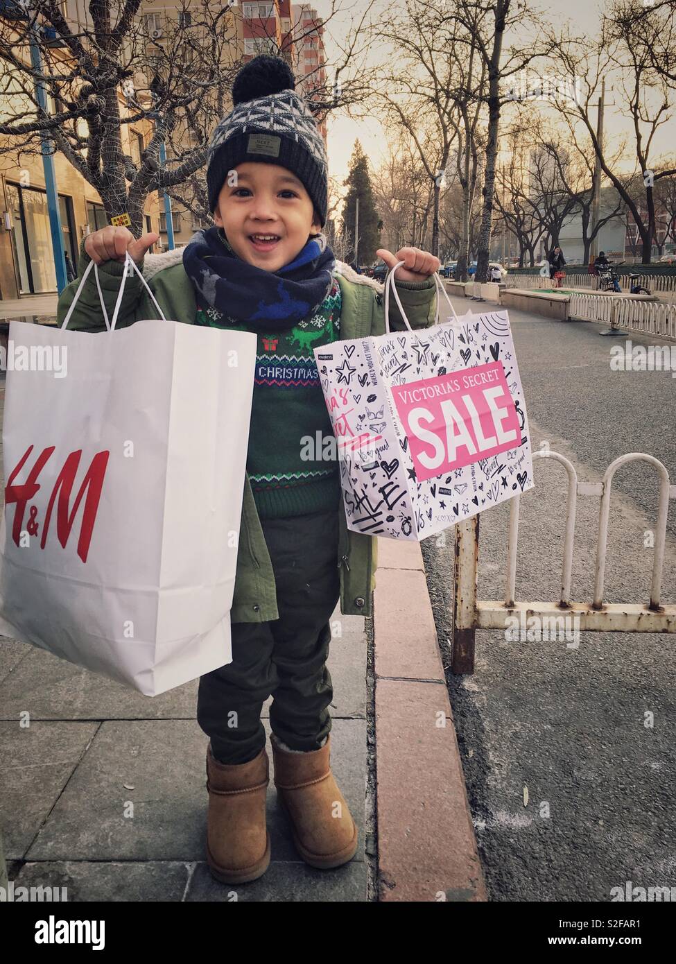 Christmas Shopping. Ein 3-jähriger Junge mit Papier Taschen Outdoor. - Smartphone-aufgenommenes Stockfoto