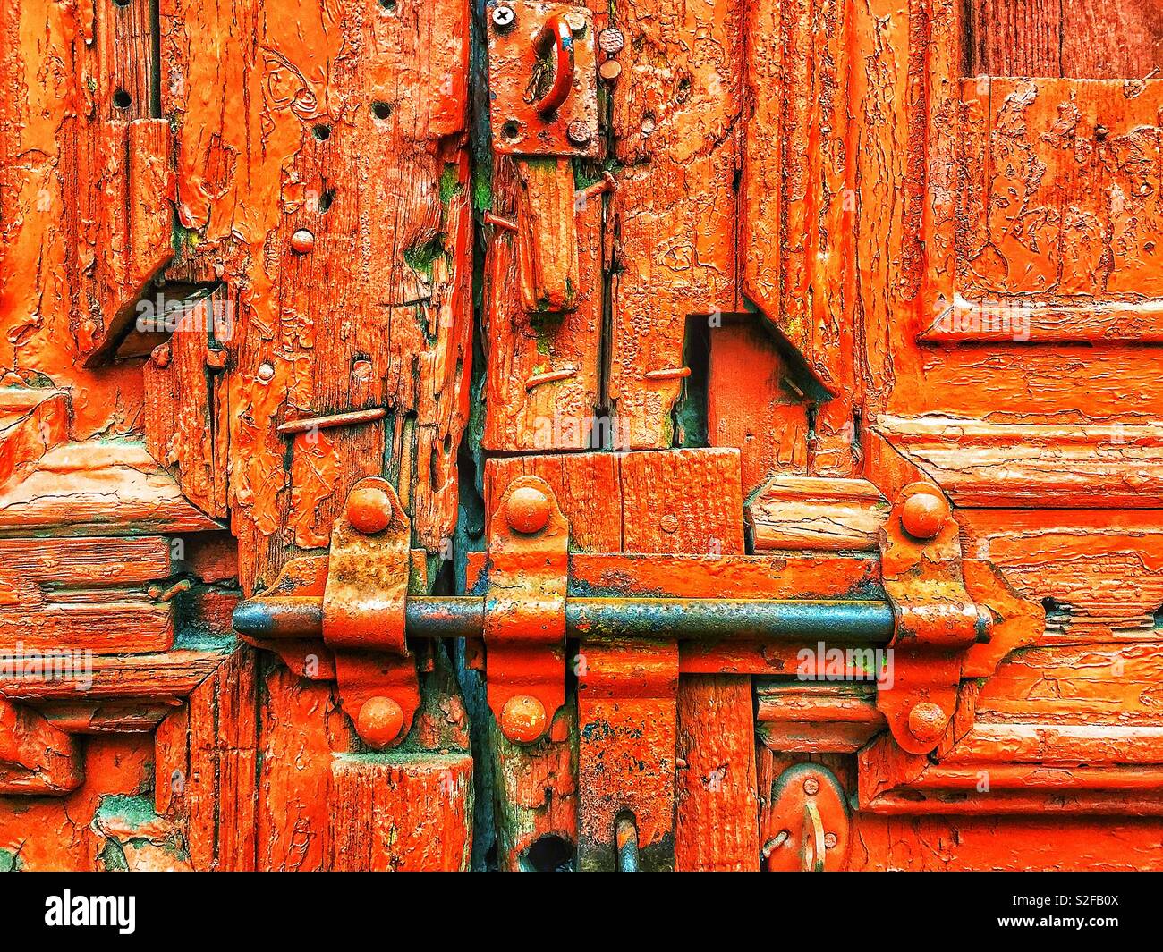 Die rostige, mit einem Vorhängeschloss verschlossene Tür mit abblätternder roter Farbe symbolisiert Einsamkeit und Verlassenheit und ruft Gefühle von Einklemmung, Vernachlässigung und Isolation hervor - Smartphone-aufgenommenes Stockfoto