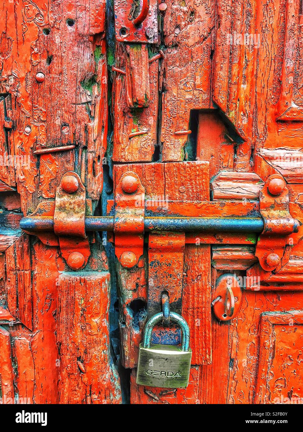 Die rostige, mit einem Vorhängeschloss verschlossene Tür mit abblätternder roter Farbe symbolisiert Einsamkeit und Verlassenheit und ruft Gefühle von Einklemmung, Vernachlässigung und Isolation hervor - Smartphone-aufgenommenes Stockfoto