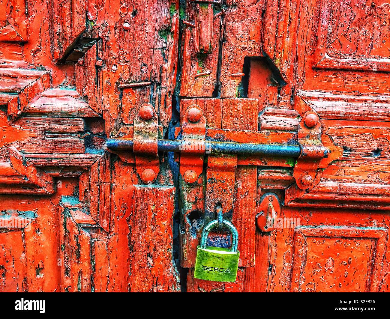 Die rostige, mit einem Vorhängeschloss verschlossene Tür mit abblätternder roter Farbe symbolisiert Einsamkeit und Verlassenheit und ruft Gefühle von Einklemmung, Vernachlässigung und Isolation hervor - Smartphone-aufgenommenes Stockfoto