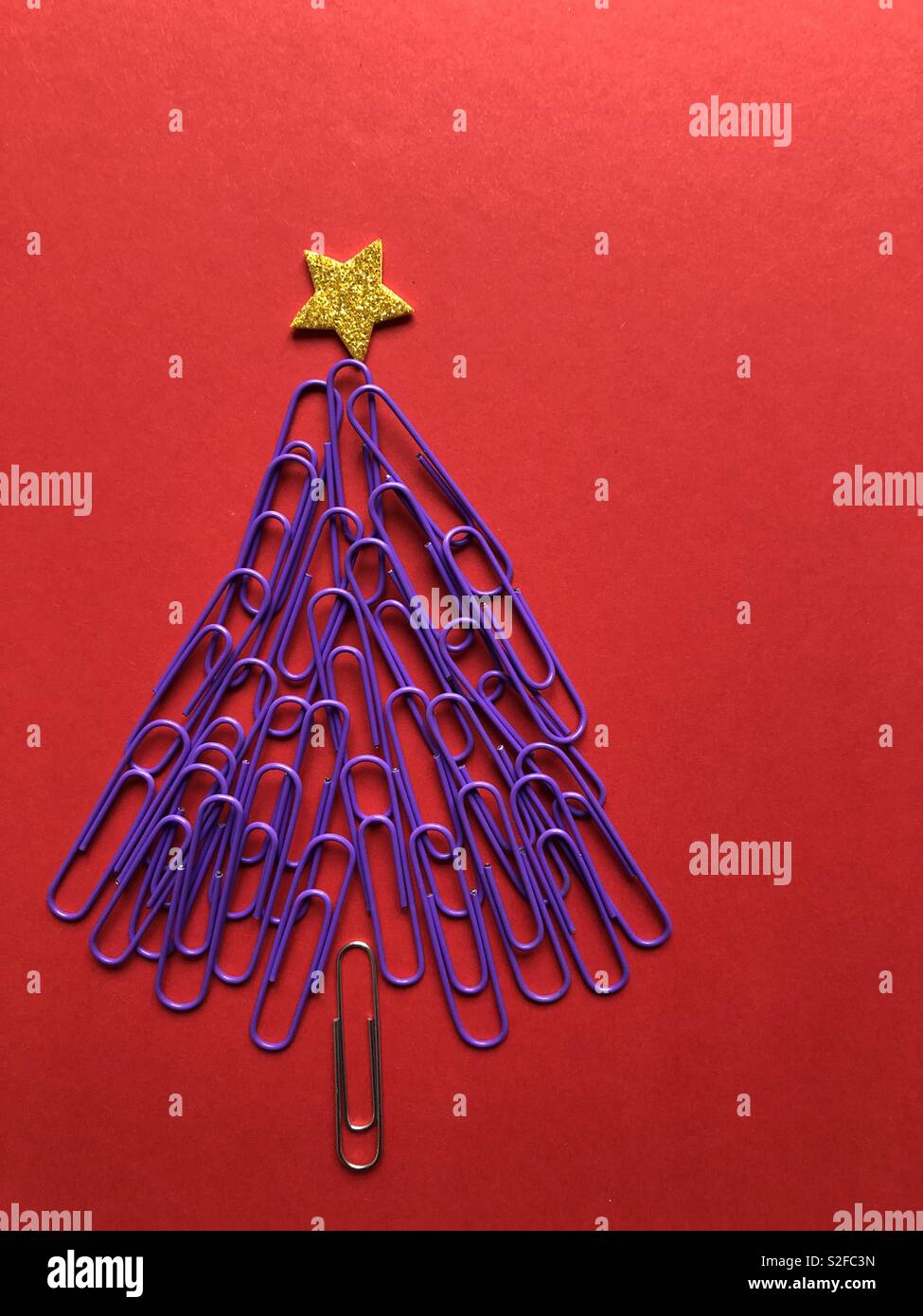 Kreative Weihnachten Konzept. Weihnachtsbaum aus lila Büroklammern gekrönt mit einem goldenen Stern auf rotem Hintergrund mit Kopie Raum Stockfoto