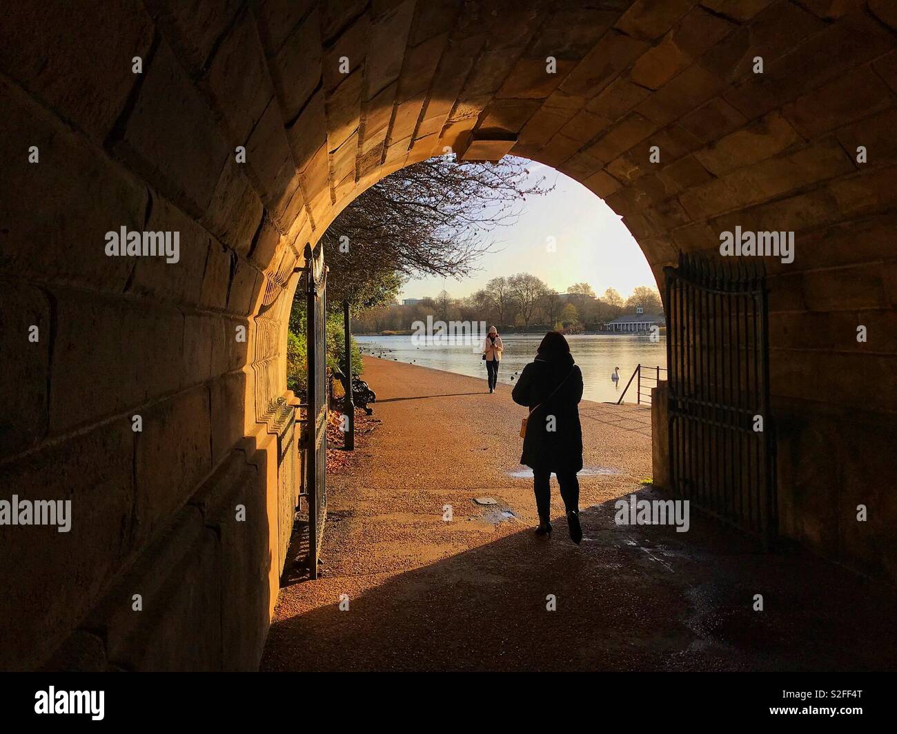 Silhouette einer Person zu Fuß neben einem See mit dem Blick, der durch die Wände eines Tunnels gerahmt Stockfoto