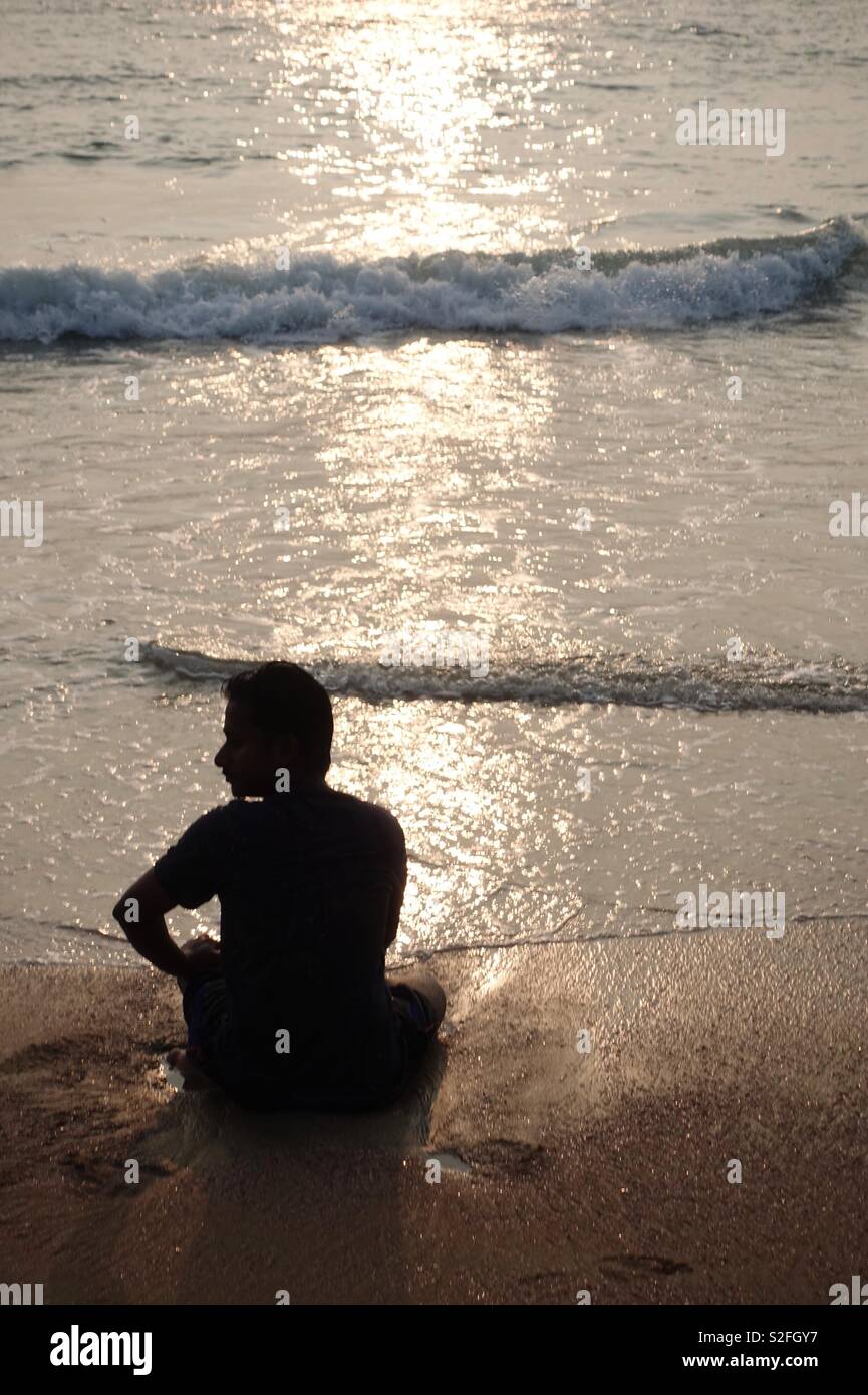 Indische Mann im Sand zu sitzen, am Strand, im Wasser beobachten die Wellen Stockfoto