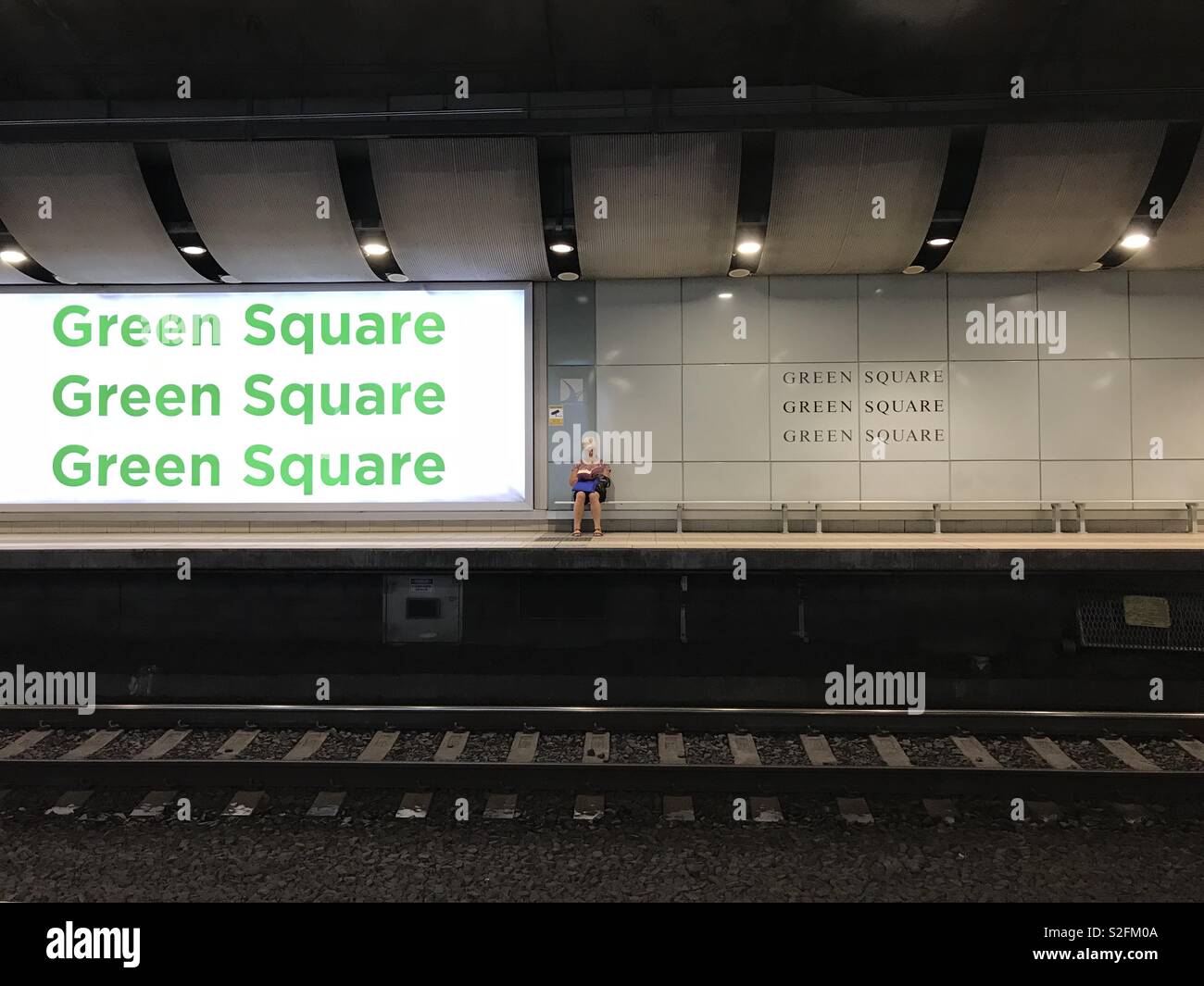 Eine Frau sitzen auf einer Bank auf dem Bahnsteig ein Buch zu lesen, wie sie für ihren Zug wartet am Grünen Platz Bahnhof in Sydney, Australien - Smartphone-aufgenommenes Stockfoto