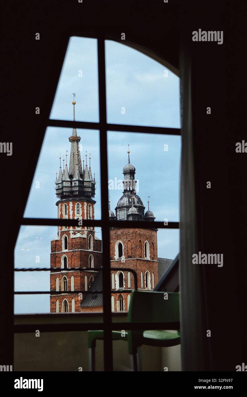 Die Türme der St. Mary's Basilica, Krakau, Polen, durch die im Obergeschoss Schlafzimmer mit Fenster des Hotel Wentzl zustimmen. - Smartphone-aufgenommenes Stockfoto
