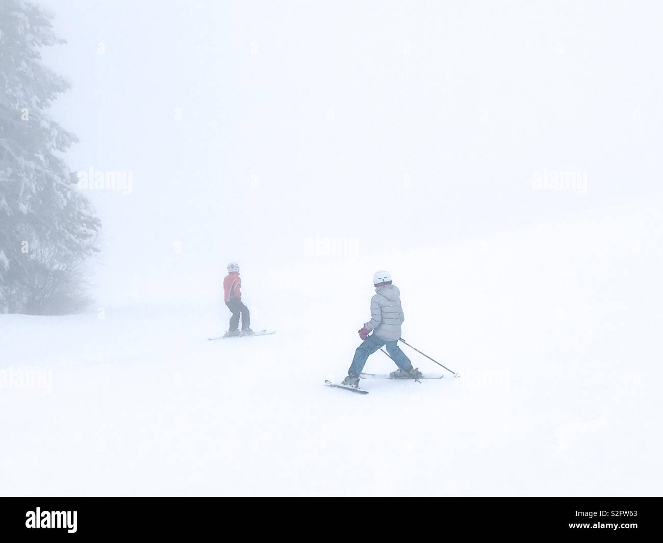 Zwei junge Skifahrer navigieren einen Skihügel in whiteout Bedingungen. Stockfoto