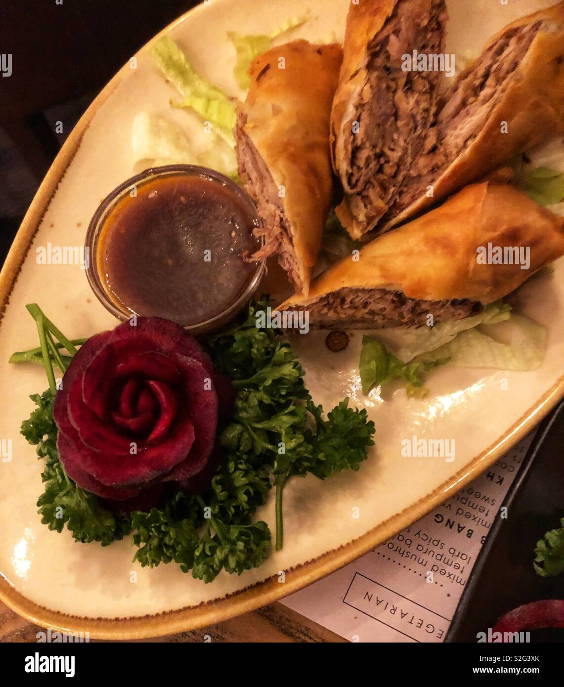 Ente Frühlingsrollen auf einer weißen Platte in ein Restaurant mit rote Beete mit Blumen auf der Seite Stockfoto