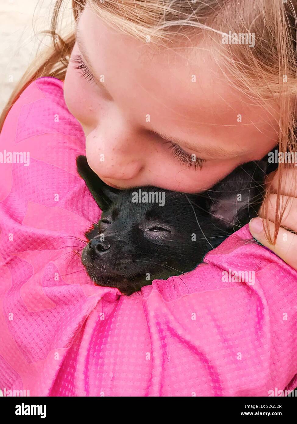 Ein Mädchen in rosa Snuggles einen kleinen schwarzen Hund. Stockfoto