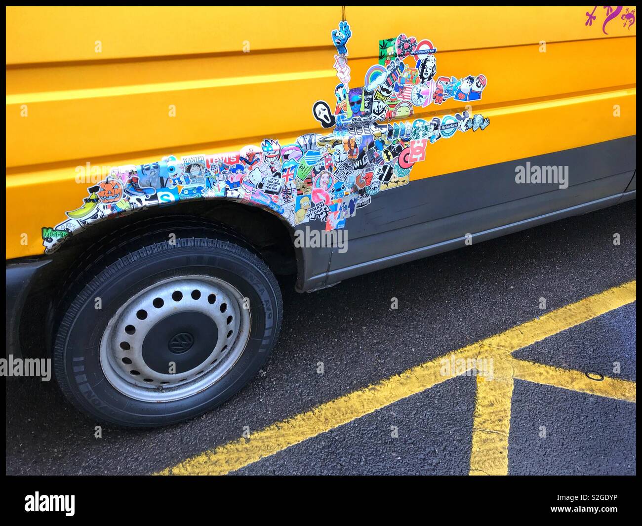 Viele kleine Bild Sticker übereinander und über dem Radkasten eines Transporters. Ist Es adverting? Es ist ein politisches Statement? Ist es nur zu flicken, etwas Rost? Gelb ist die dominierende Farbe. Stockfoto