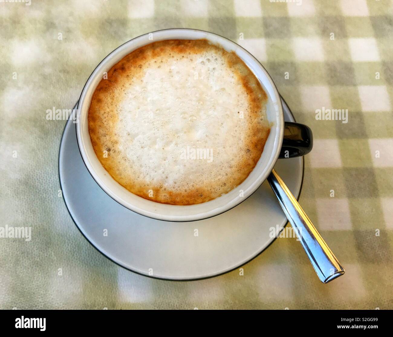 Cremiger latte Kaffee in eine Tasse und Untertasse auf einem karierten Tischtuch Stockfoto