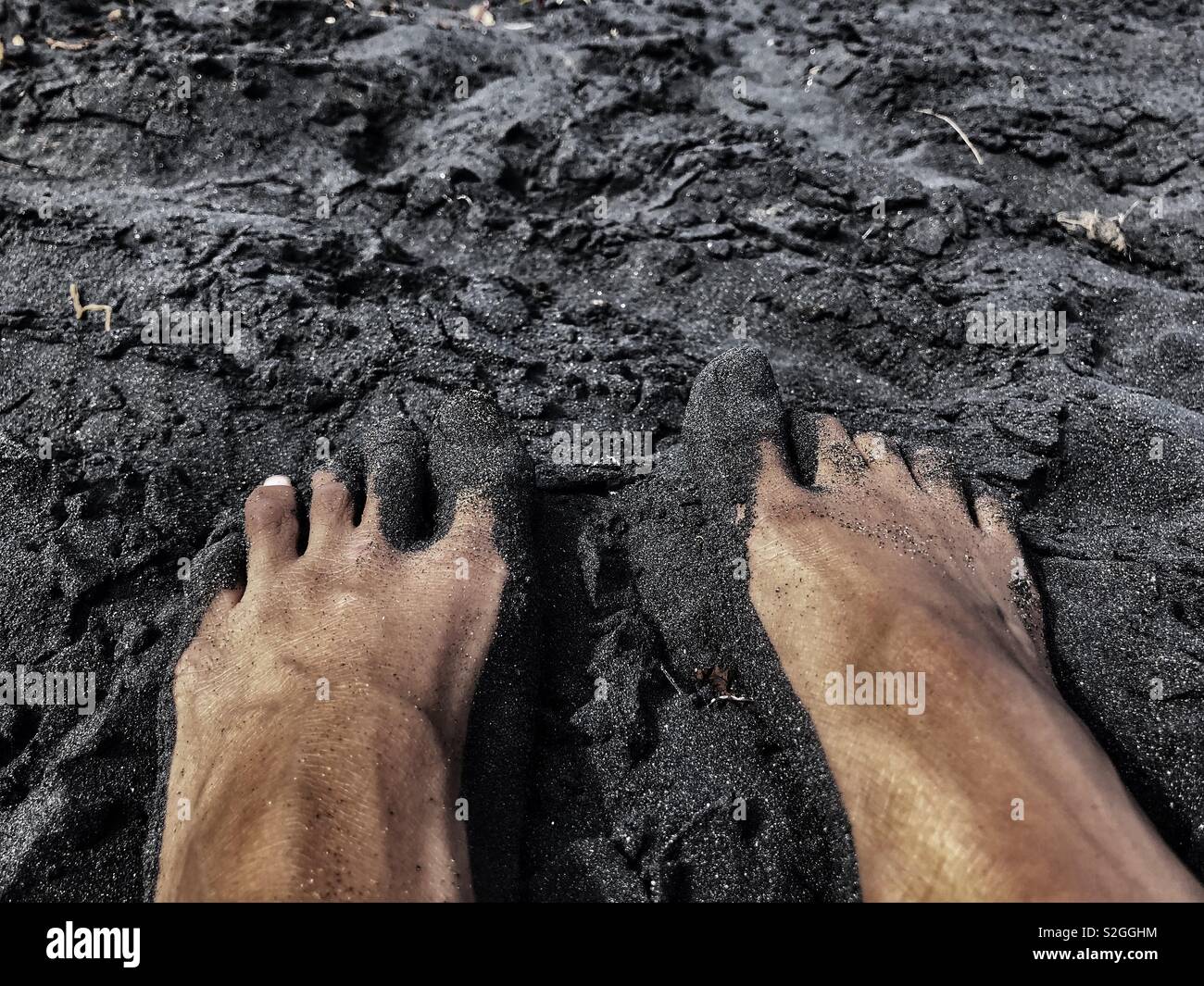 Ein Paar Füßen auf schwarzem Sand Stockfoto