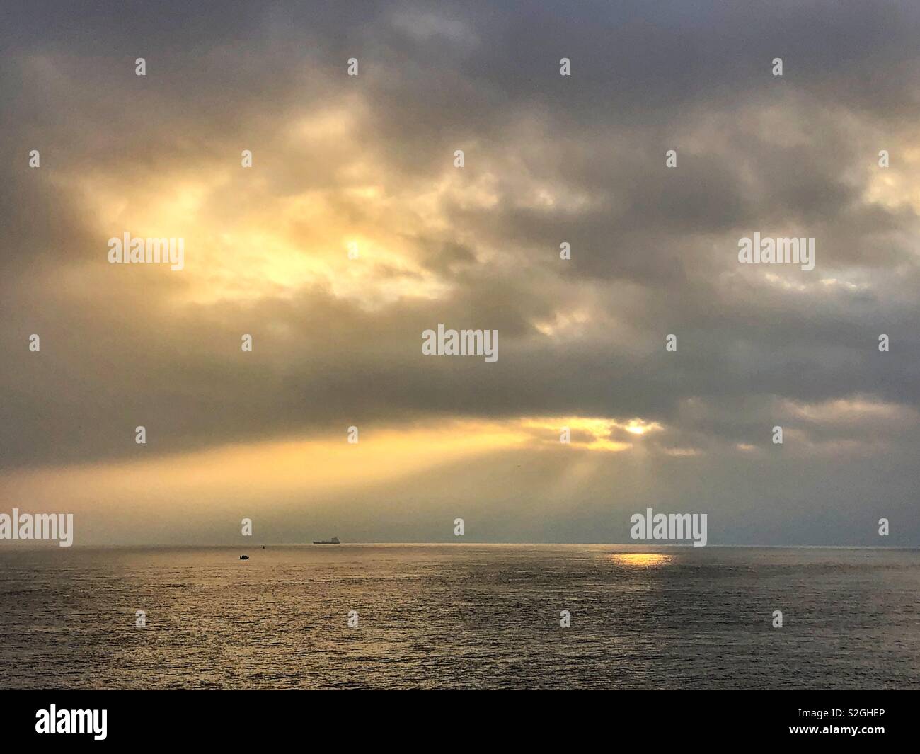 Sunburst durch dicke Wolken über dem Meer mit Sonnenstrahlen. Stockfoto