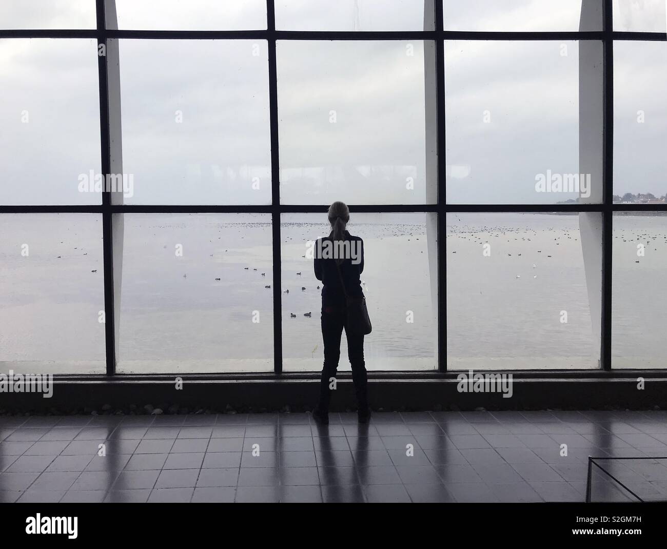 Person im Silhouette aus der Ferne stehend gesehen und Suchen aus einem riesigen Fenster Abschnitt Stockfoto
