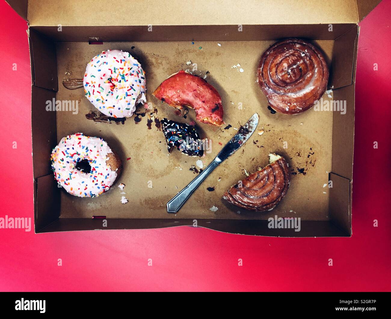 Halb leere Box mit übrig gebliebenem Donuts auf Rote Tabelle Stockfoto