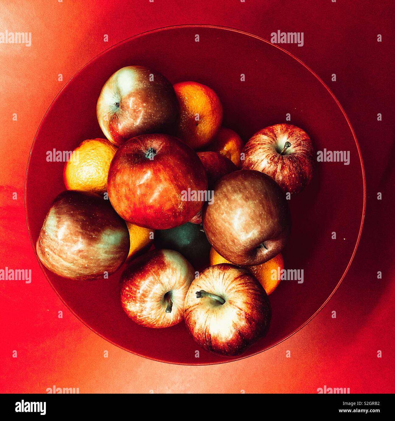 Rote Schale mit roten Äpfeln und Orangen auf dem roten Tisch Ansicht von oben Stockfoto