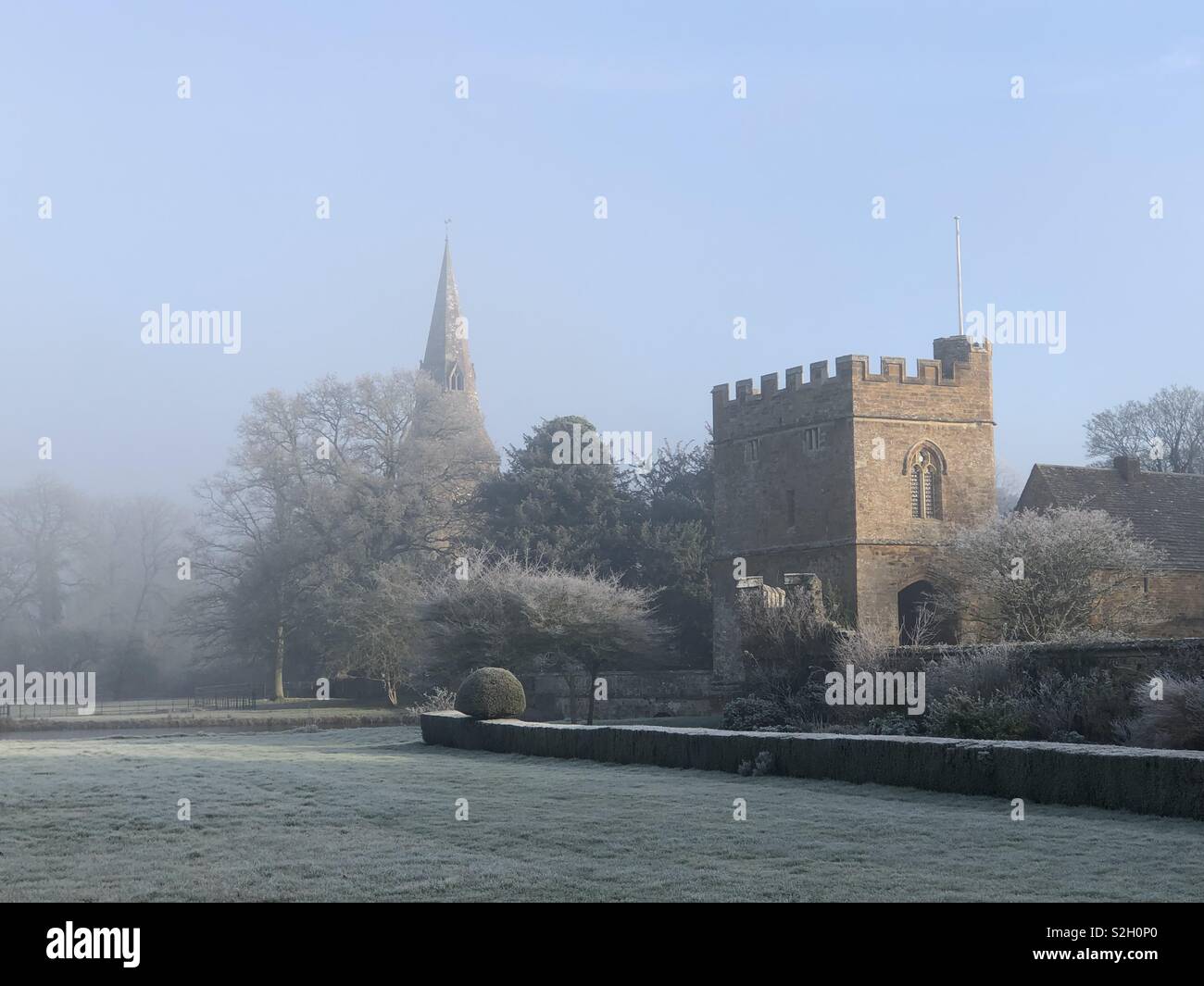 Broughton Schloss Torhaus mit Pfarrkirche Turm gegen einen schönen blauen Himmel umrahmt und in einer Winterlandschaft nach dem härtesten Frost des Jahres. Stockfoto