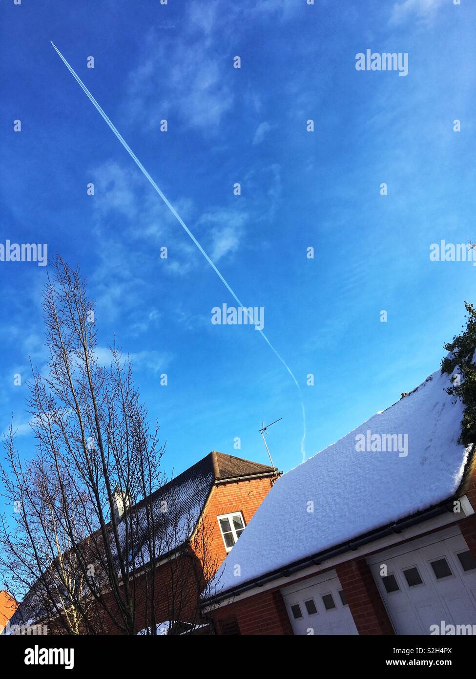 Von schräg Dächer mit Schnee, mit einer hohen Ebene mit diagonalen Dampf Zug in einem blauen Himmel. Kopieren Sie Platz. Stockfoto