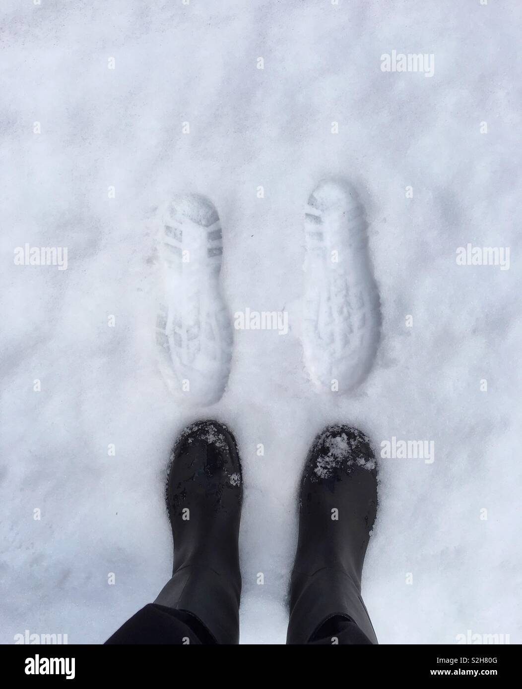 Der untere Teil ein Paar Beine in schwarzen Hosen und Gummistiefel, vor zwei Spuren im Schnee. Platz kopieren Stockfoto