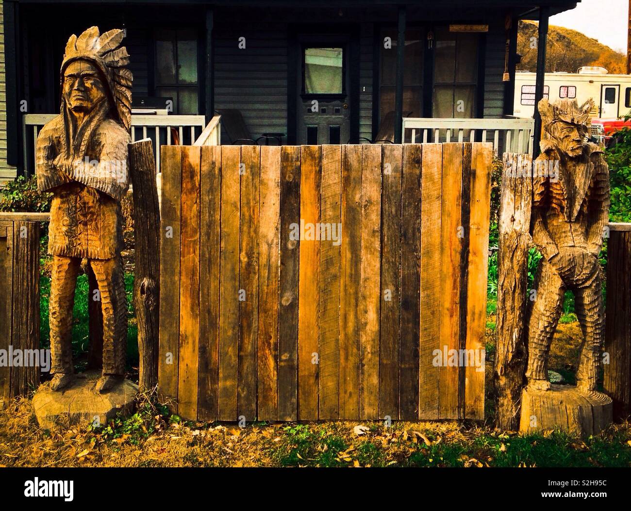 Hölzerne Statue der mürrische Indian Chief mit verschränkten Armen und mürrisch Cowboy mit Händen in den Taschen der geschnitzten stehen auf jeder Seite der hölzernen Tor vor dem Haus Stockfoto