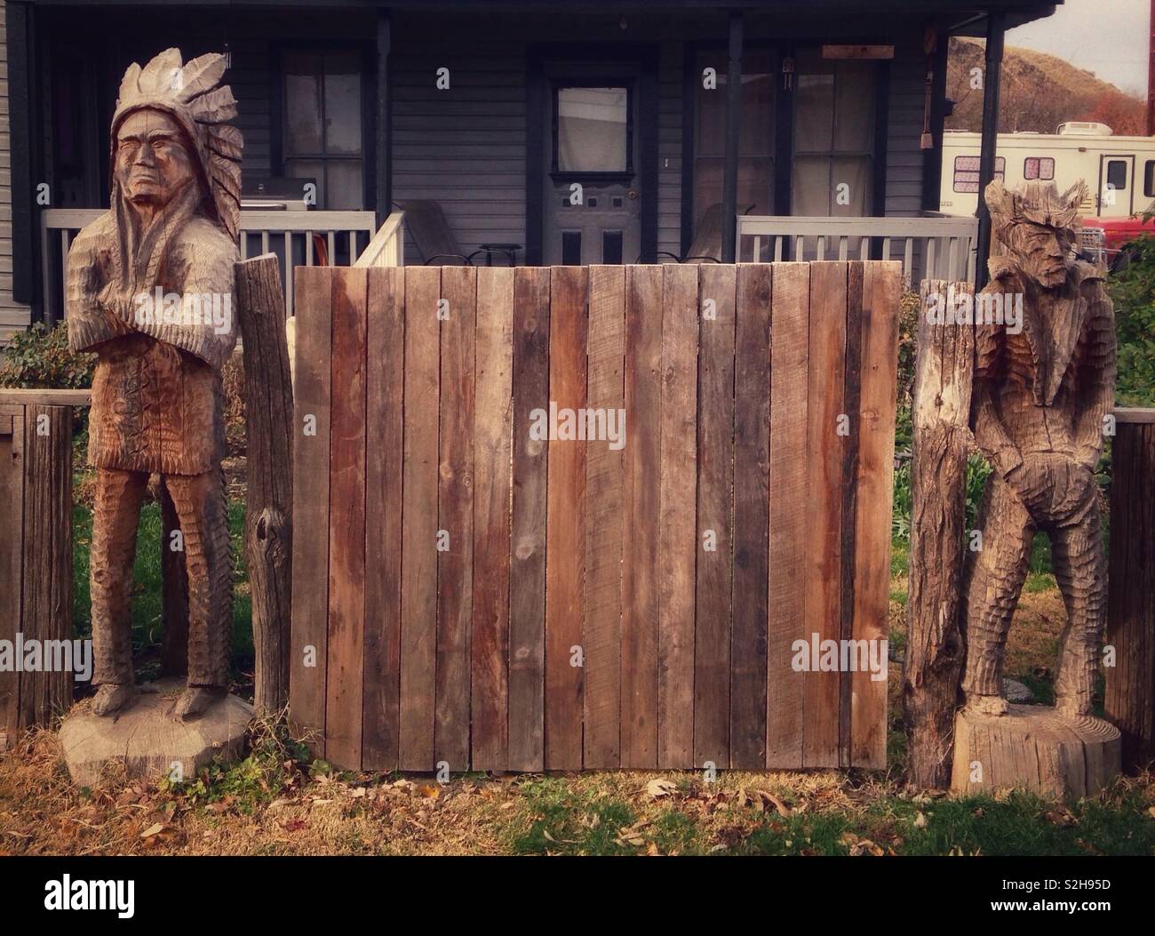 Mürrische Holz- Indian Chief mit verschränkten Armen und mürrisch Holz- Cowboy mit Händen in den Taschen stehen auf beiden Seiten des hölzernen Tor vor dem Haus Stockfoto