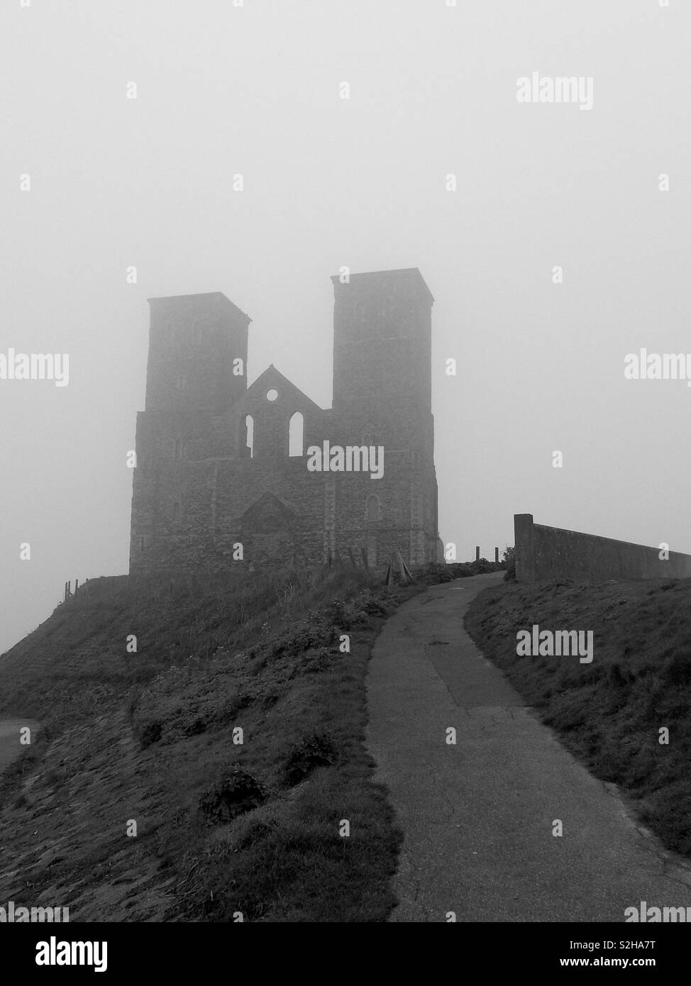 Eine stimmungsvolle Aussicht auf die berühmten Wahrzeichen und Twin Towers der Ruinen von Reculver Kirche, Kent, drohende Aus einem Meer Nebel. Stockfoto