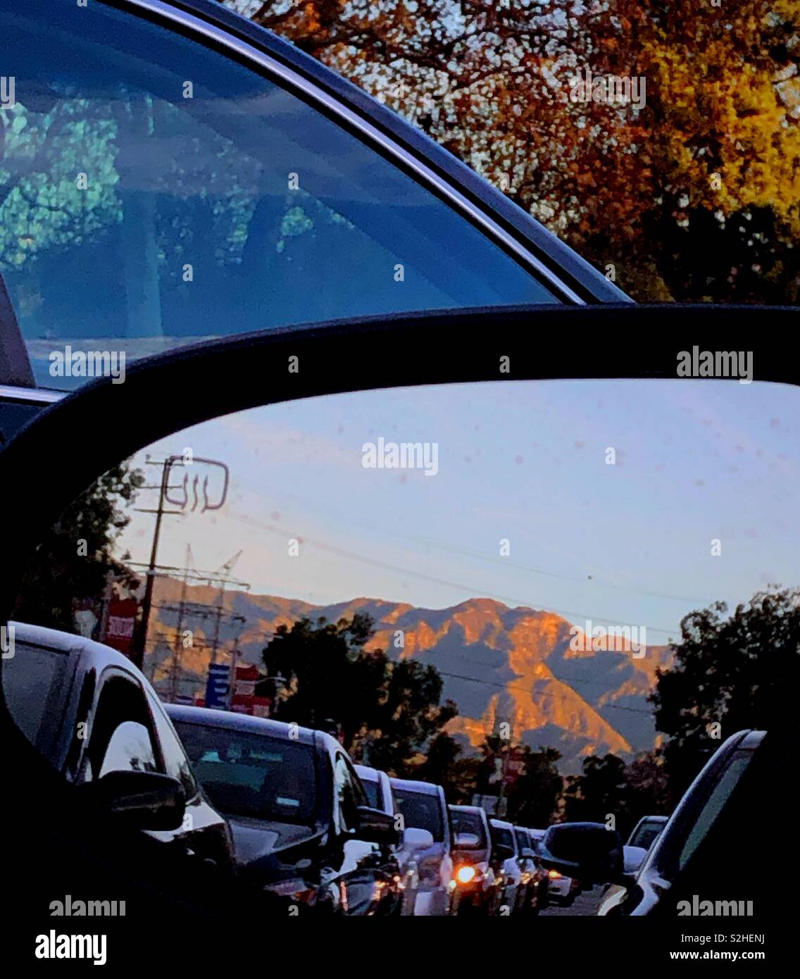 Rush hour Staus auf der Autobahn, als er Sonnenuntergang Farben der umliegenden Ausläufer - alle in einem Spiegel reflektiert. Stockfoto
