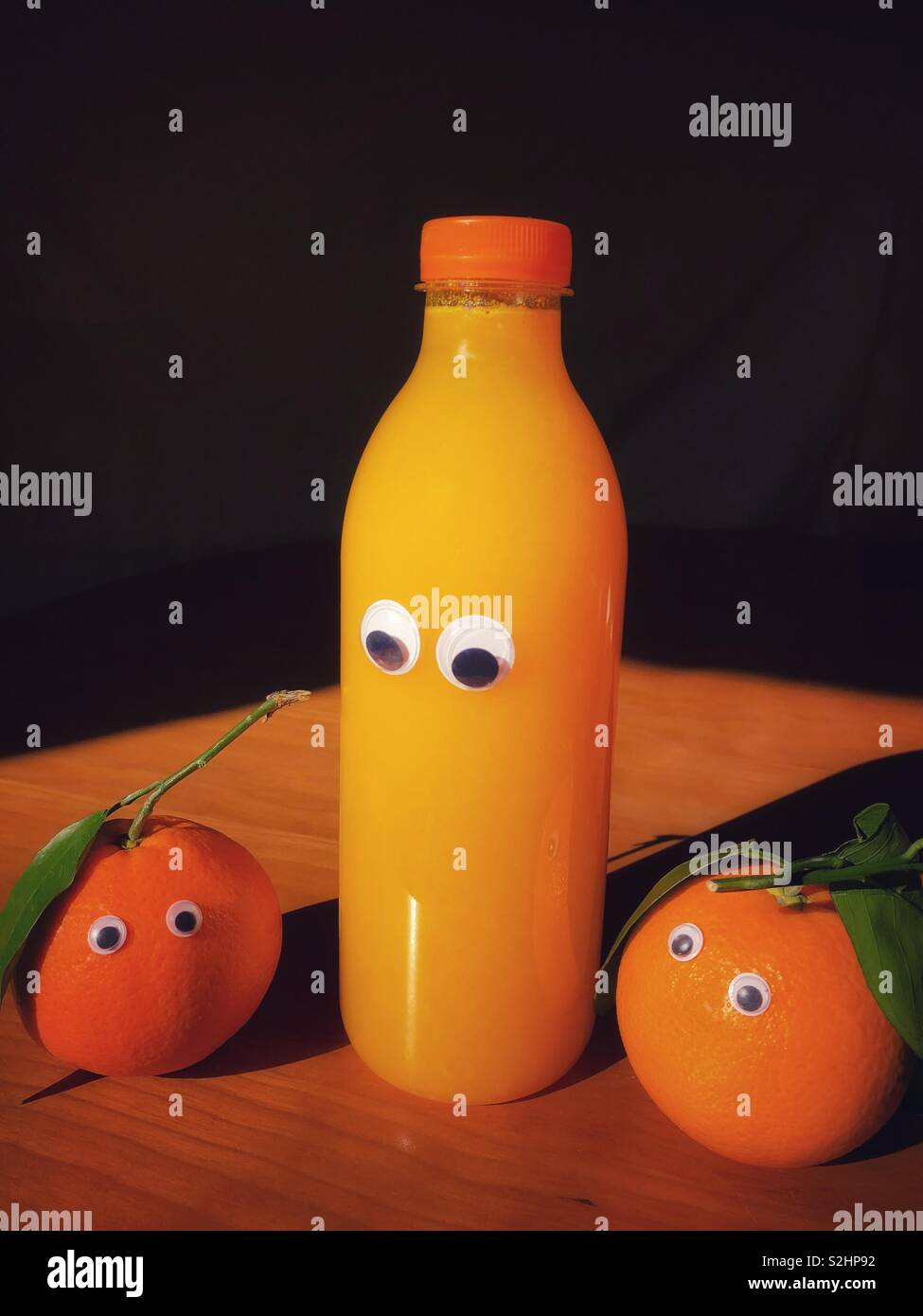 Kreative spaß essen: Organische Orangen mit Google Augen neben einem googly eyed Flasche frisch gepresster Orangensaft - Smartphone-aufgenommenes Stockfoto