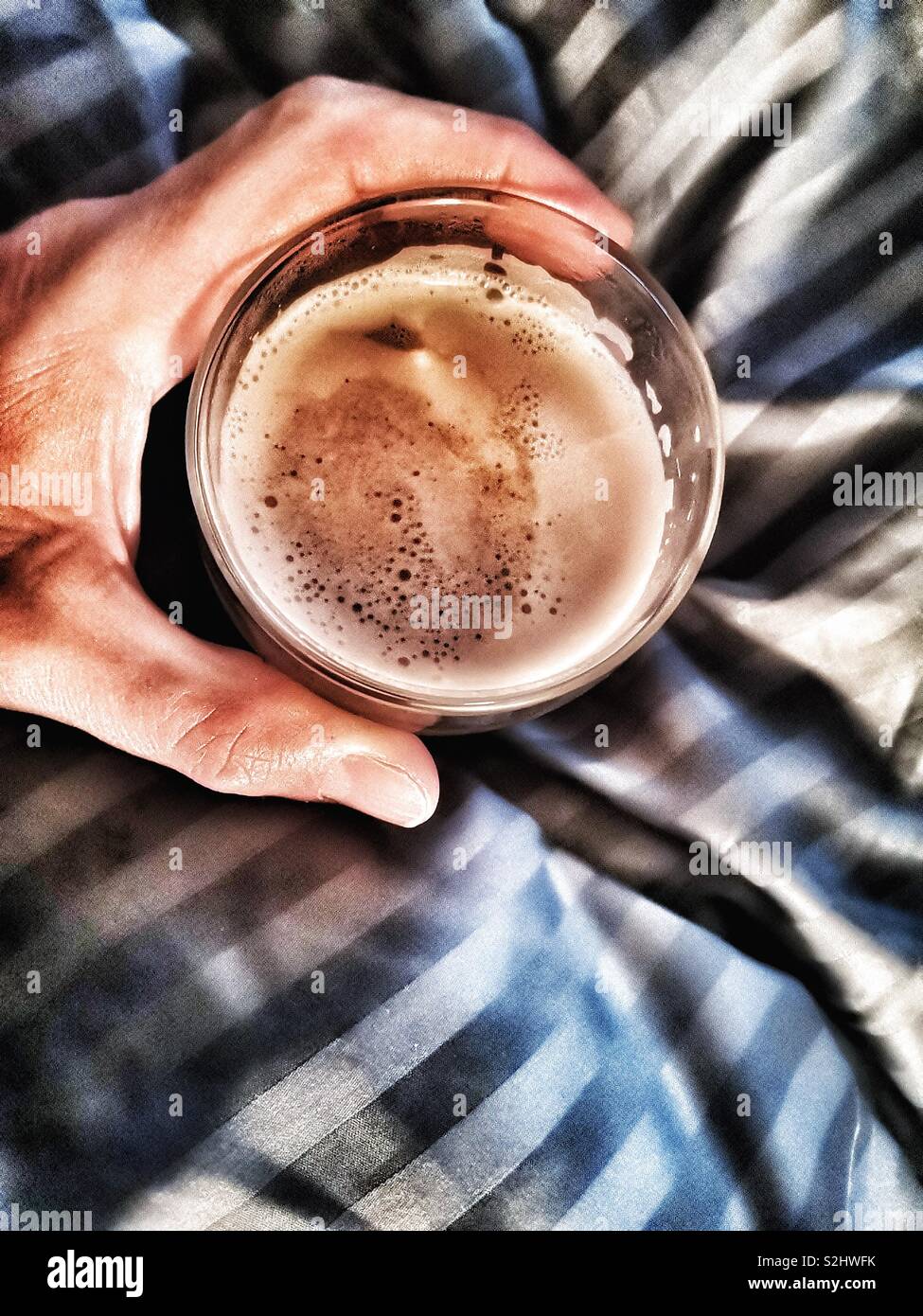 Blick von oben auf die Hand des Menschen halten Glas Cafe Latte im Bett - Smartphone-aufgenommenes Stockfoto