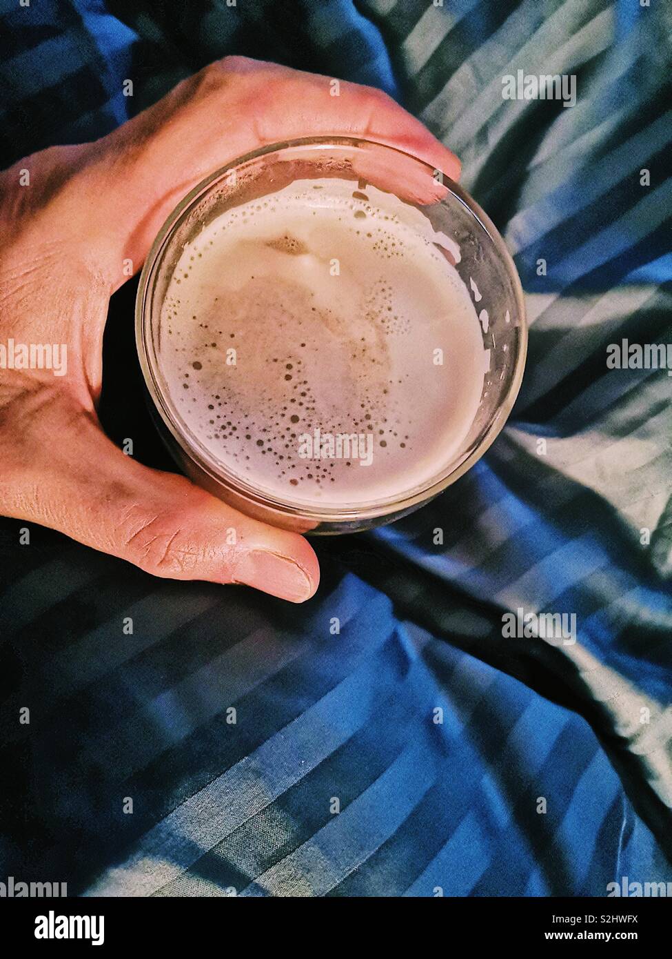 Ansicht der Hand Mann hält Glas Cafe Latte im Bett - Smartphone-aufgenommenes Stockfoto