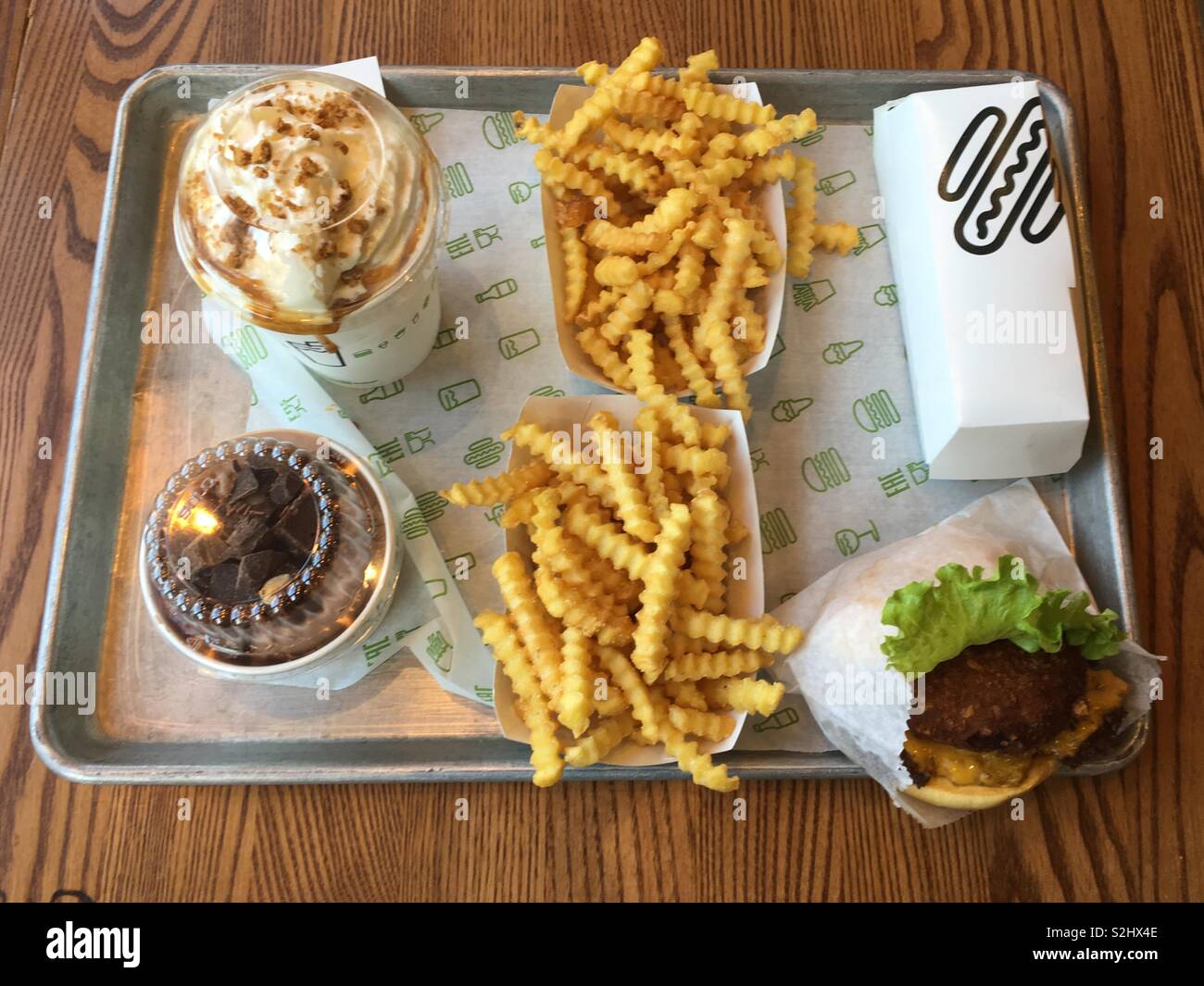 Ein Tablett mit Essen aus der Shake Shack. Apfelkuchen Milchshake mit einem Chocolate Brownie Beton Eis. Crinkle cut Chips ein Stapel Burger und Hot Dogs. Stockfoto