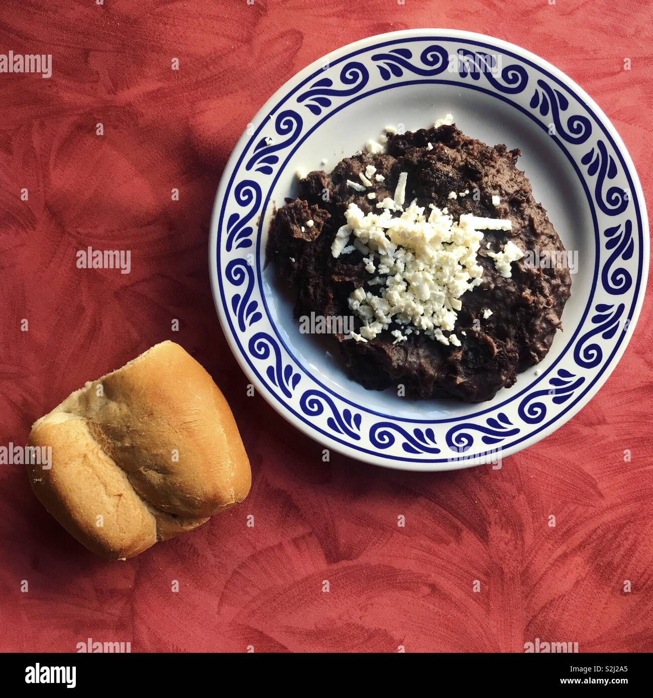 Schwarze Bohnen mit Käse in einer verzierten Keramik Platte und ein Stück Brot auf einem roten Tisch in Santa Clara Restaurant in Puebla, Mexiko - Smartphone-aufgenommenes Stockfoto