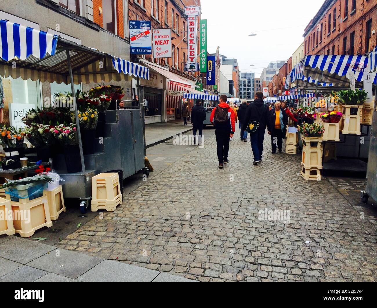 Auf der Suche einer gepflasterten Gasse oder Straße auf einem grauen kalten Herbst Tag in der Stadt von Dublin in Irland mit blumenverkäufer und Fußgänger - Smartphone-aufgenommenes Stockfoto