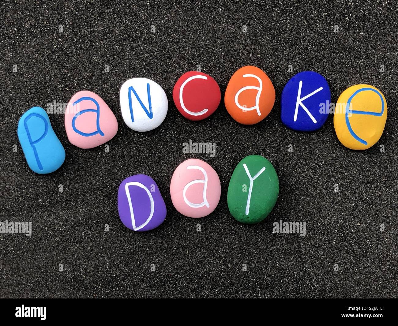 Pancake Day gefeiert mit einer Komposition aus bunten Meer Steine über schwarzen vulkanischen Sand Stockfoto