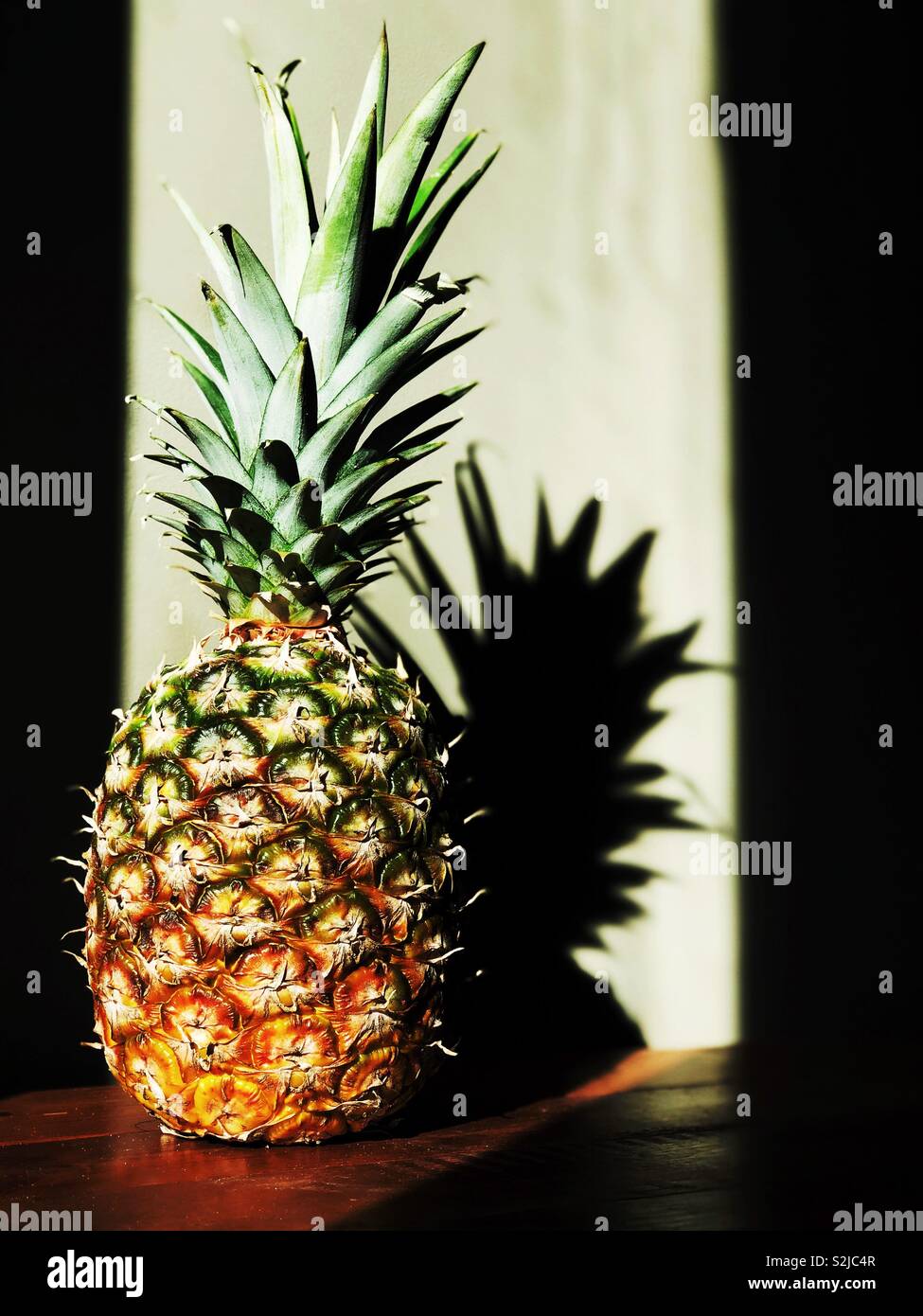 Ganze Ananas im Sonnenlicht auf Holz- Oberfläche werfen Schatten Stockfoto