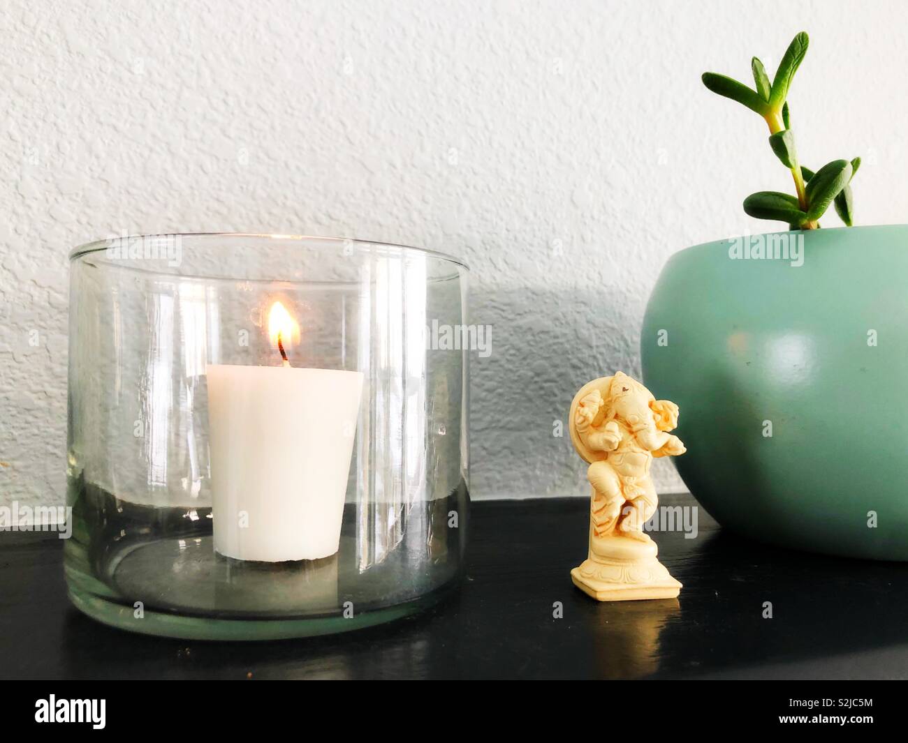 Eine brennende Kerze neben einem kleinen Ganesha Figur und eine sukkulente Pflanze. Stockfoto
