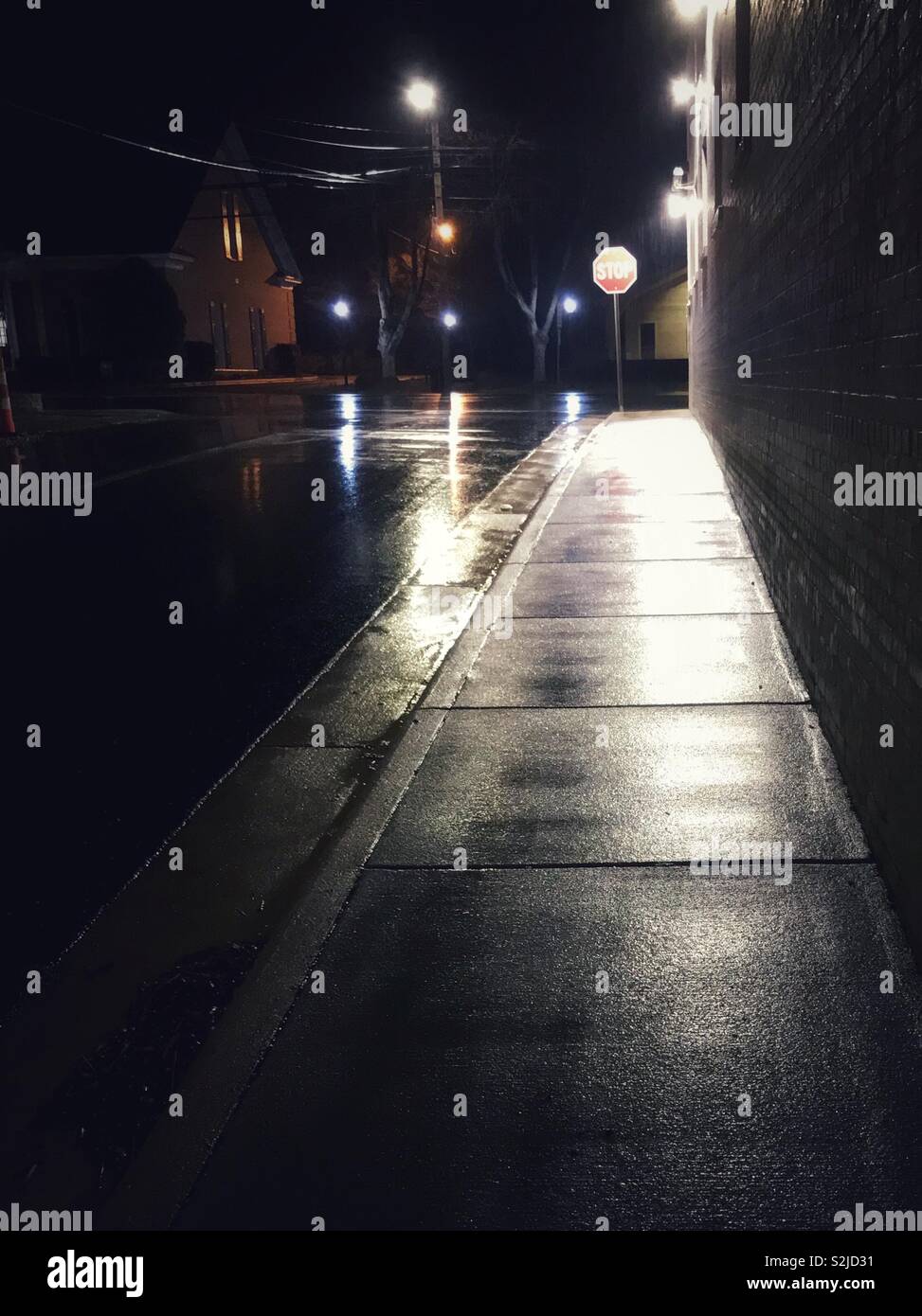 Regen durchnässt Bürgersteig spiegelt Straßenlaterne nach Einbruch der Dunkelheit Stockfoto