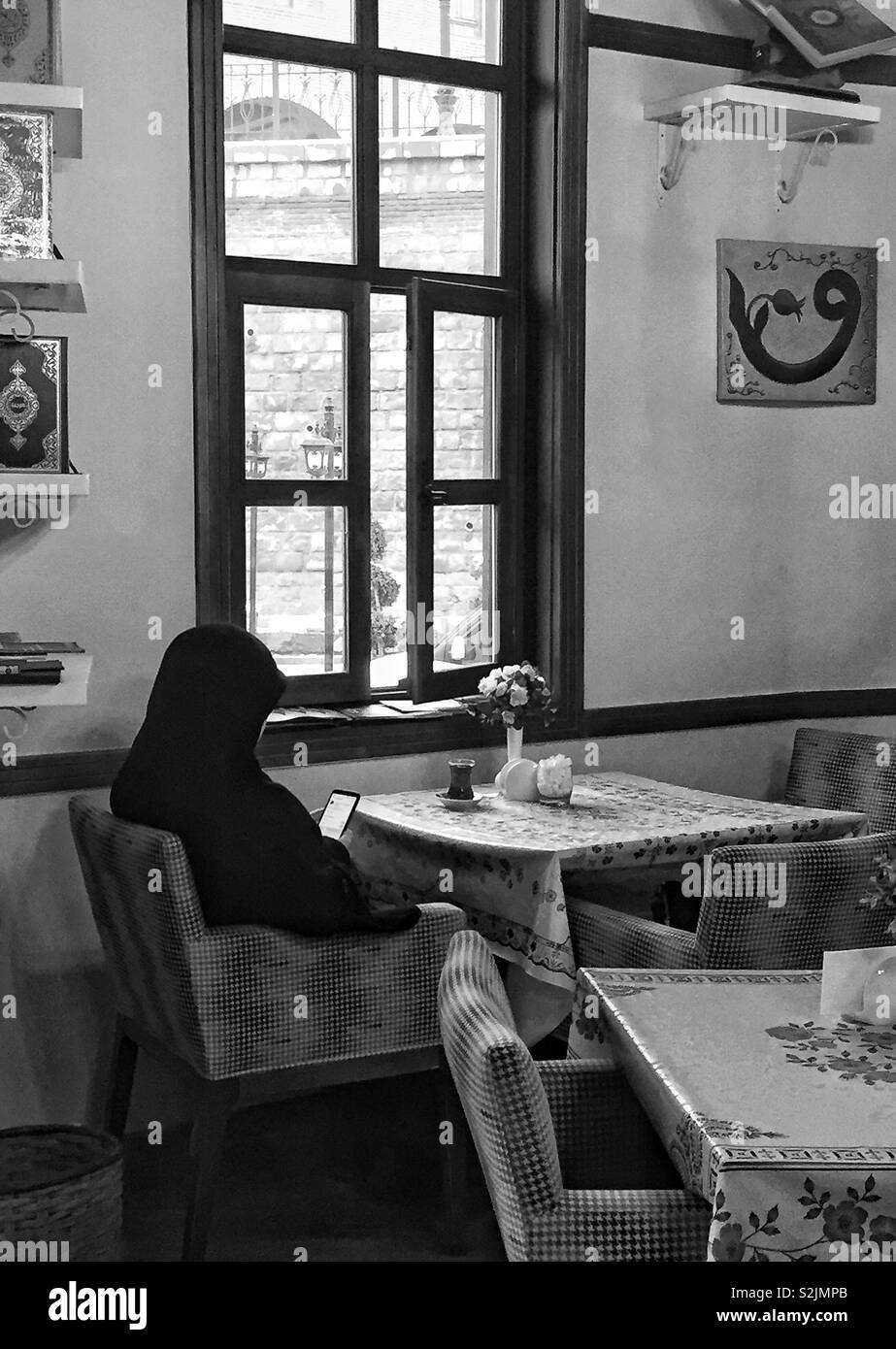 Muslimische Frau in Schwarz mit Smartphone in ihrer Hand im Cafe Tabelle in Ankara, Türkei gekleidet Stockfoto