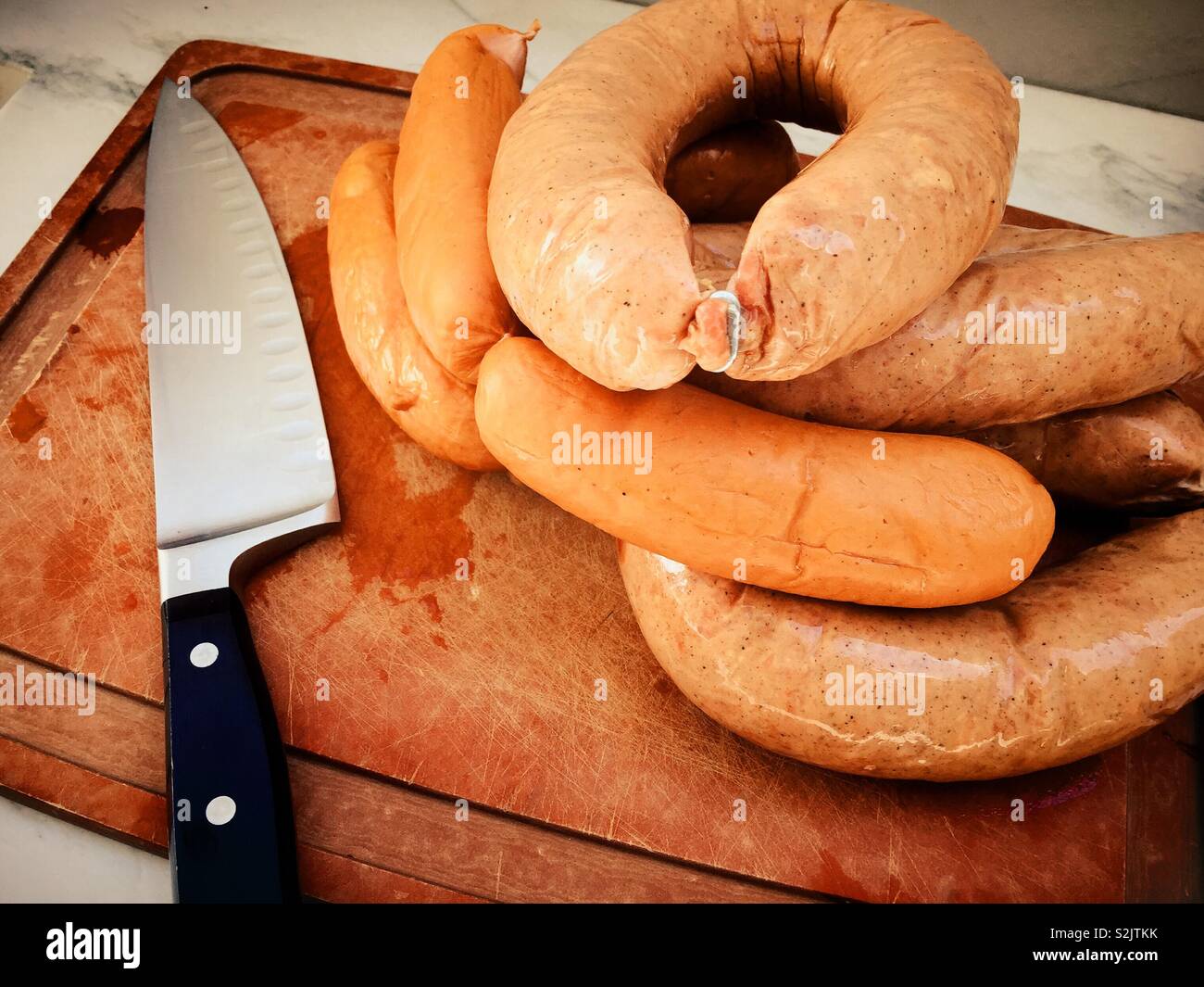 Schneidbrett und Messer mit Kielbasa und knockwurst Würstchen. - Smartphone-aufgenommenes Stockfoto