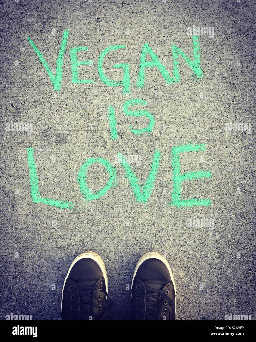 Füße in grüne Schuhe auf der Suche nach veganen Nachricht an Bürgersteig geweißt. Stockfoto