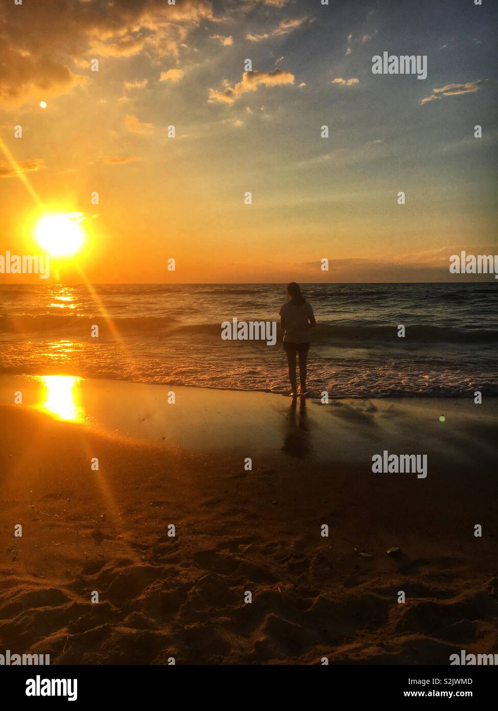 Schöne junge Frau an den Rand des Wassers und geniessen Sie einen schönen Sonnenuntergang. Stockfoto