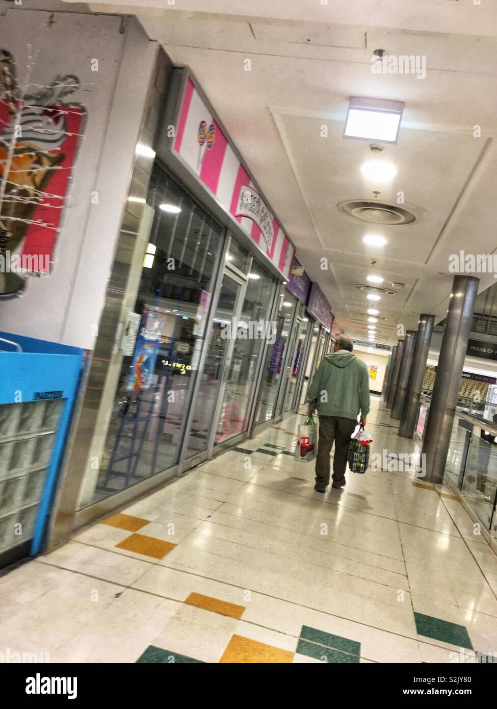 Ein älterer Mann, mit zwei Einkaufstaschen, Fuß in hell beleuchteten Einkaufszentrum. Stockfoto