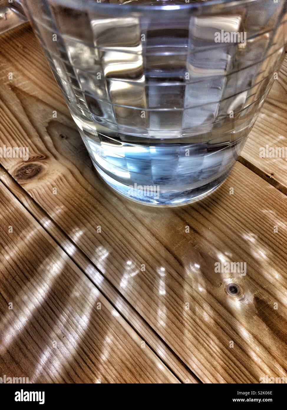 Glas Wasser beleuchtet Erzeugen von Mustern von Licht, Holz Hintergrund - Smartphone-aufgenommenes Stockfoto