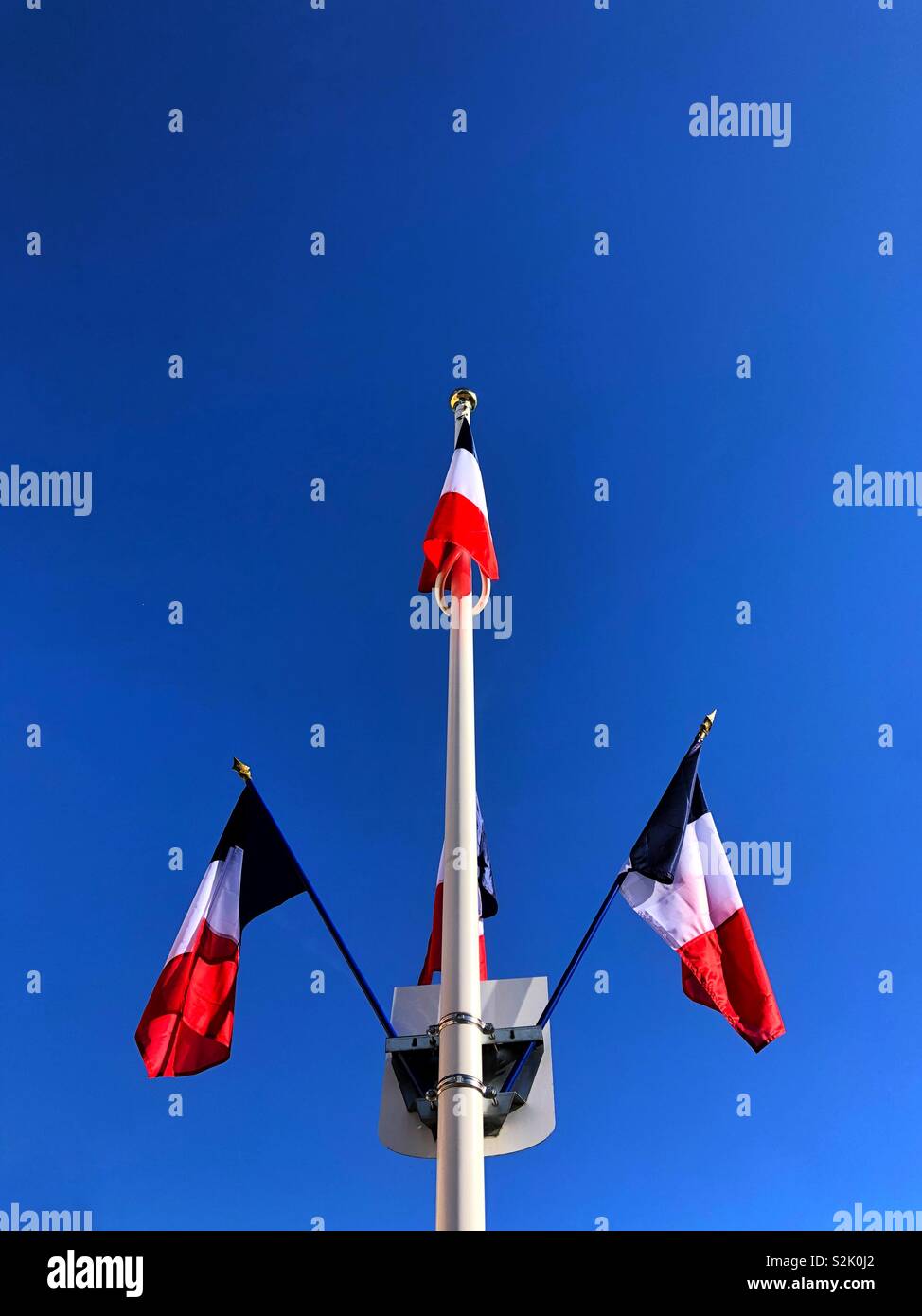 Drei dreifarbige Fahnen hängen von einem Fahnenmast in der Rue, Hauts-de-France vor blauem Himmel Stockfoto