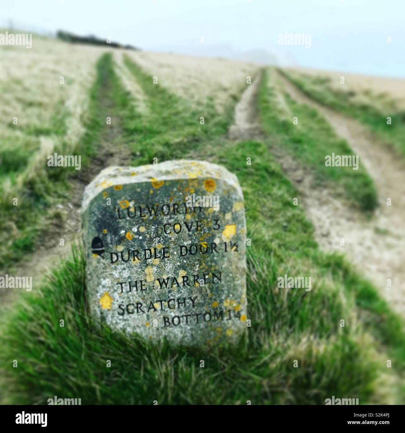 Markierungsstein auf dem South West Coast Path mit Klippen in der Ferne Stockfoto