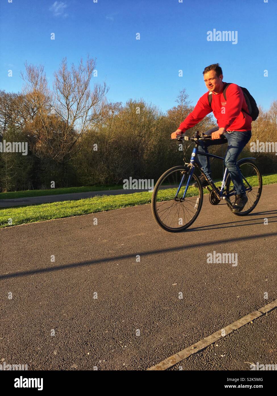 Ein Mann im roten Pullover Freilauf, auf einem Fahrrad auf einen Weg in einem bewaldeten Park. Platz kopieren Stockfoto