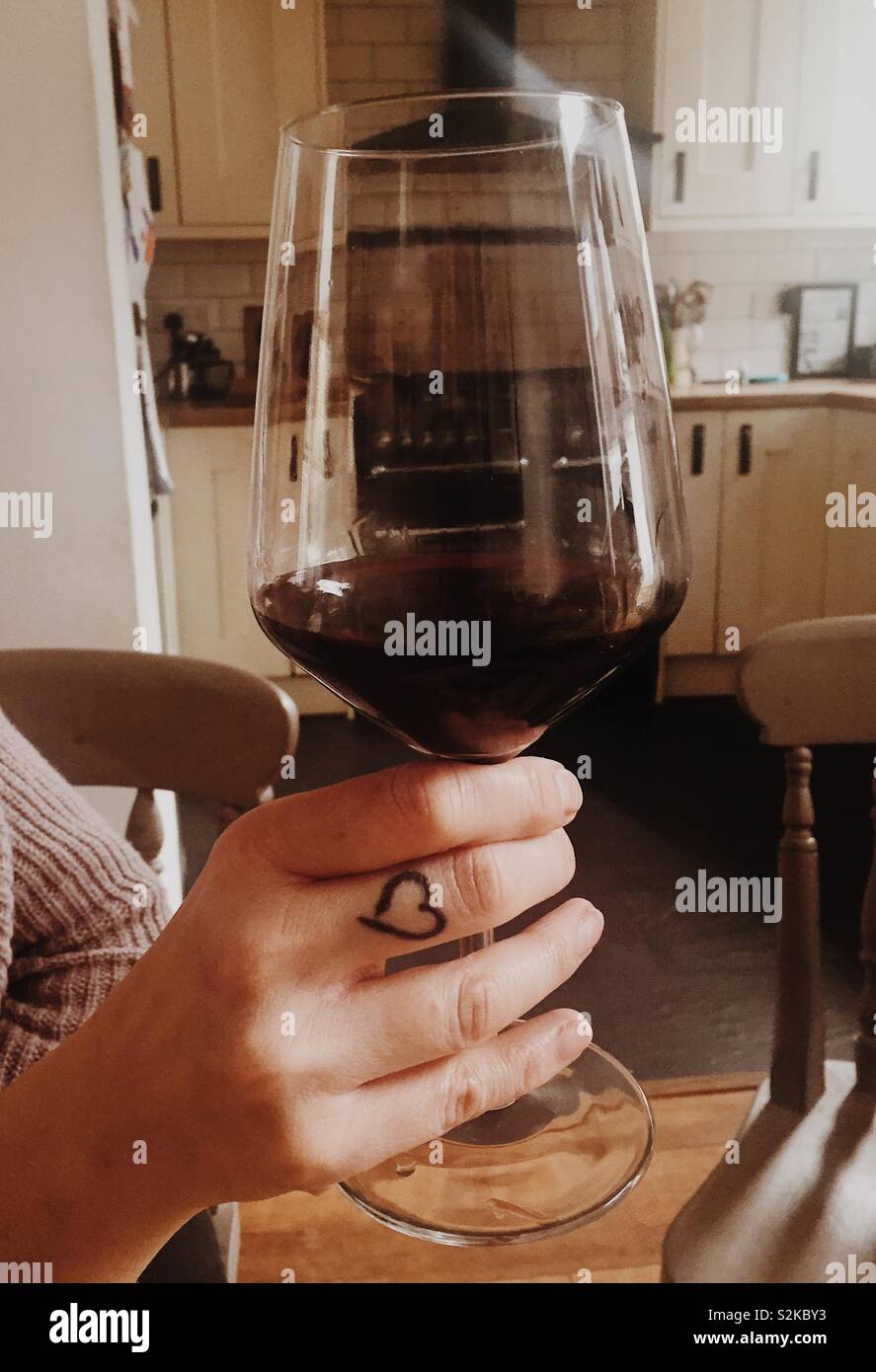 Frau mit einem Glas Rotwein in der Hand mit Herz tattoo - Smartphone-aufgenommenes Stockfoto