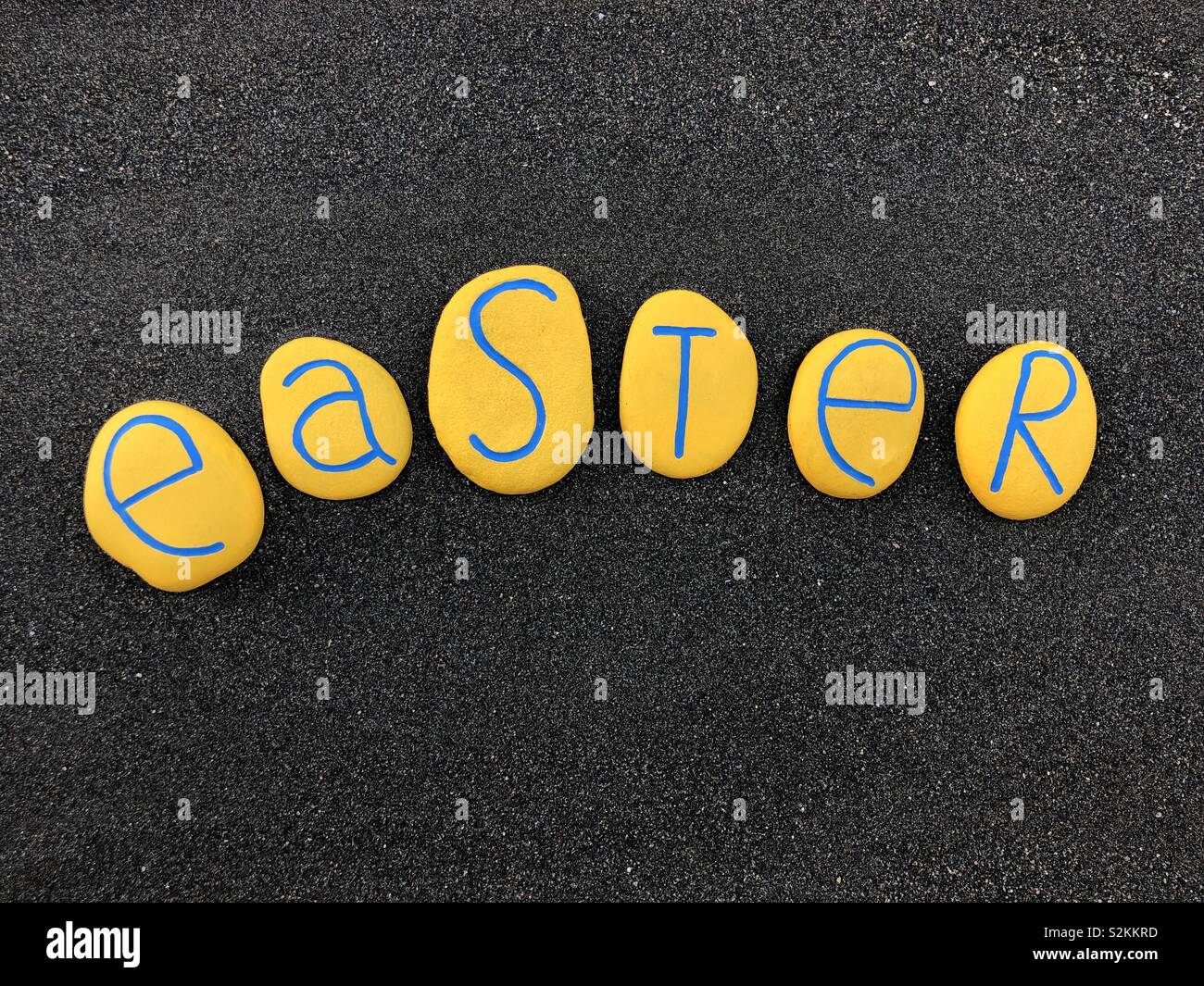 Ostern Text mit Gelb bemalten Steinen über schwarzen vulkanischen Sand Stockfoto