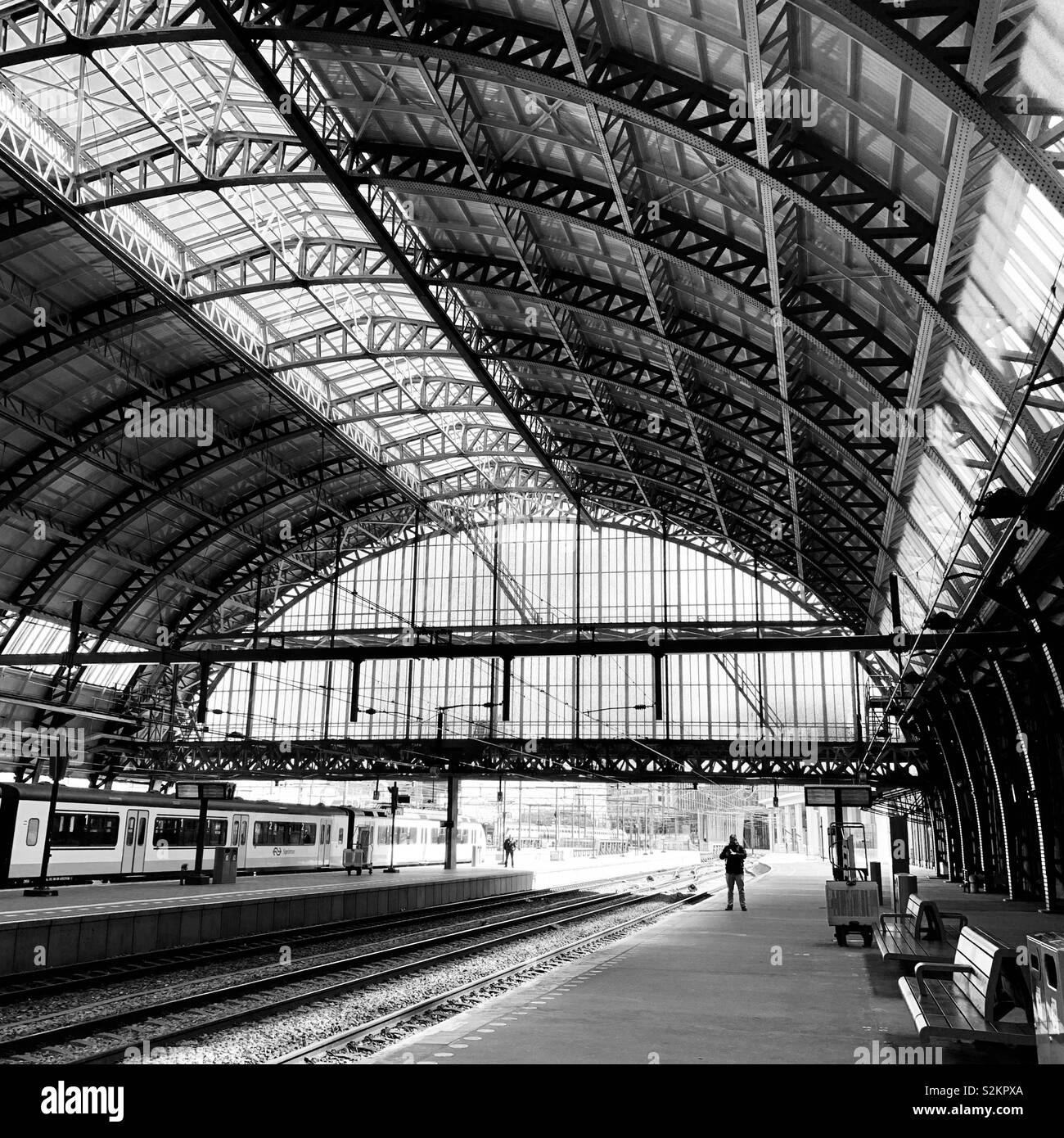 Amsterdam, Niederlande, 12. April 2019: Ein Mann wartet auf einen Zug auf einer verlassenen Plattform an der Central Station. - Smartphone-aufgenommenes Stockfoto