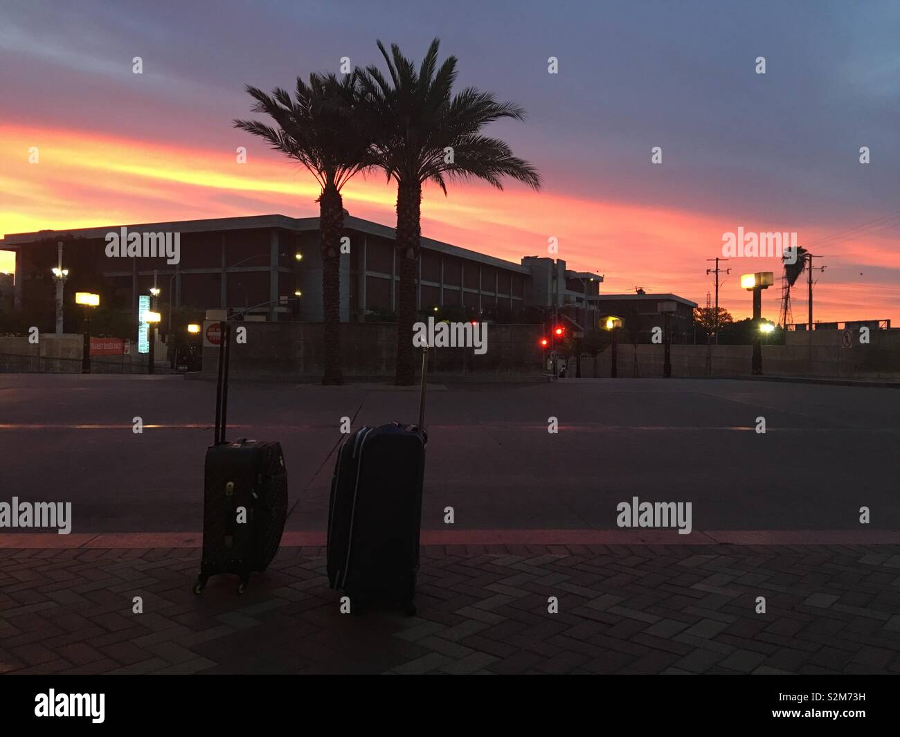 LOS ANGELES, Ca, APRIL 2019: zwei Koffer an leeren Straßenkante, Patsouras Transit Plaza außerhalb der Union Station in der Innenstadt. Kurz vor Sonnenaufgang mit Silhouette Palmen und Orange Sky Stockfoto