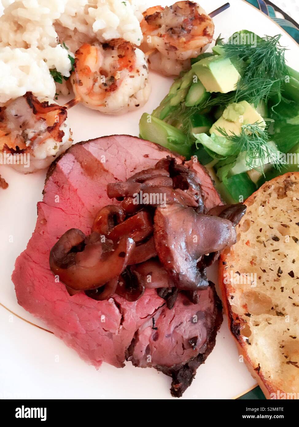 Flach Nahaufnahme von einer ausgewogenen Mahlzeit von Rinderfilet, Garnelen, Knoblauchbrot und Salat, USA Stockfoto